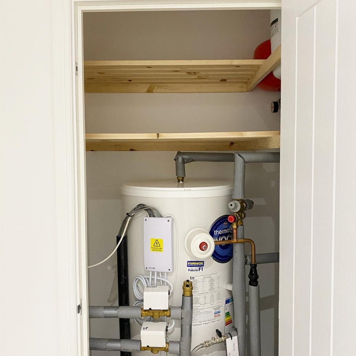 Wooden slatted shelves installed on the walls above a white hot water tank in a cupboard.