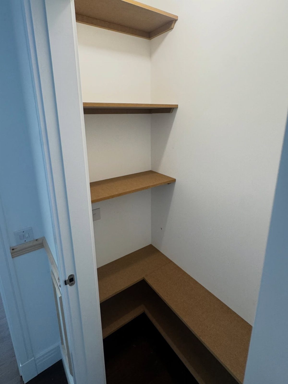 Empty wooden shelves installed inside a white cupboard against white walls.