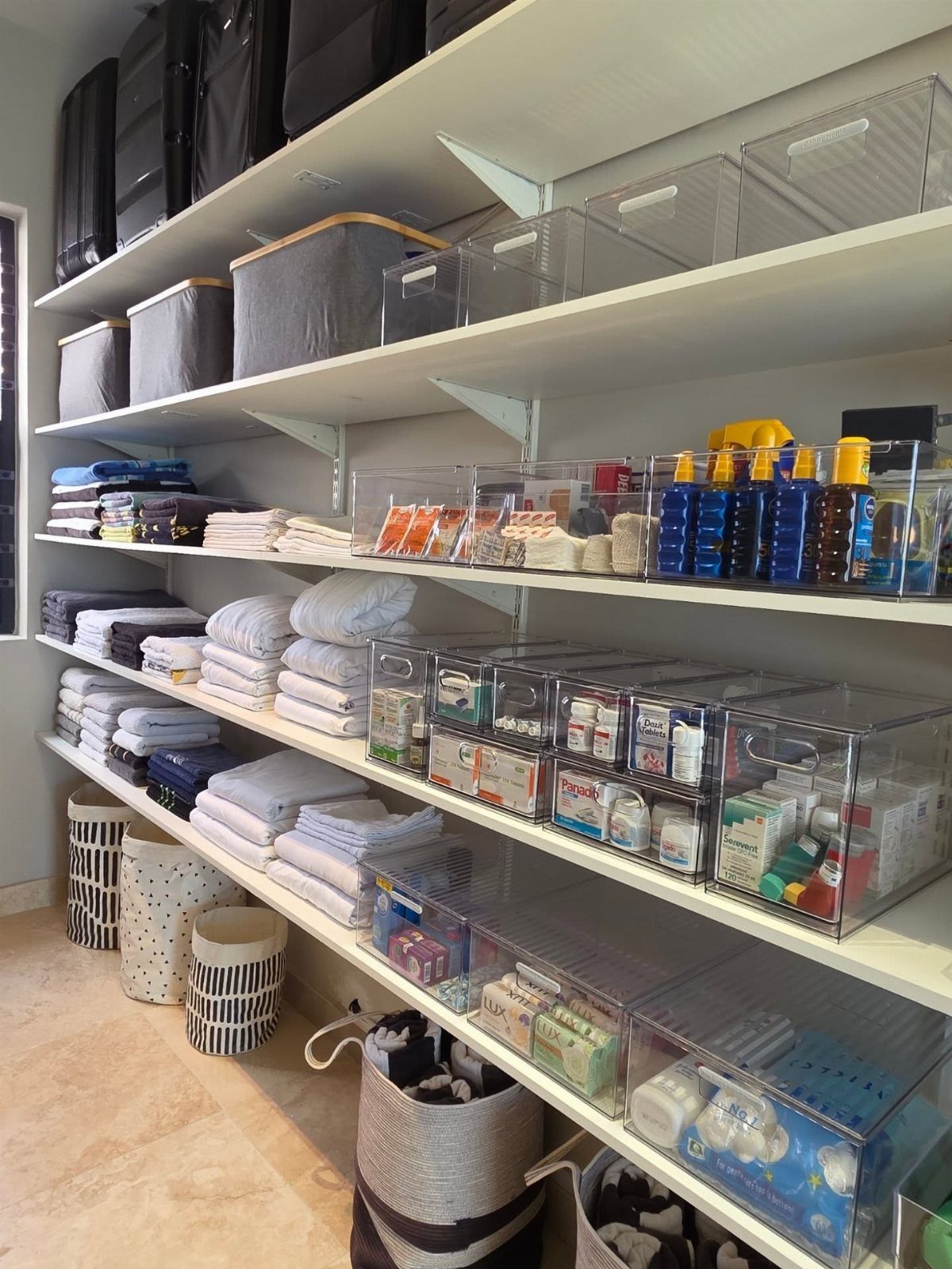 White open shelves organized with folded linens, clear storage bins, and fabric boxes in a bright room.