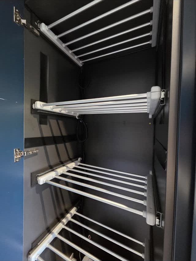 White slatted pull-out drying racks installed inside a dark blue storage cupboard.