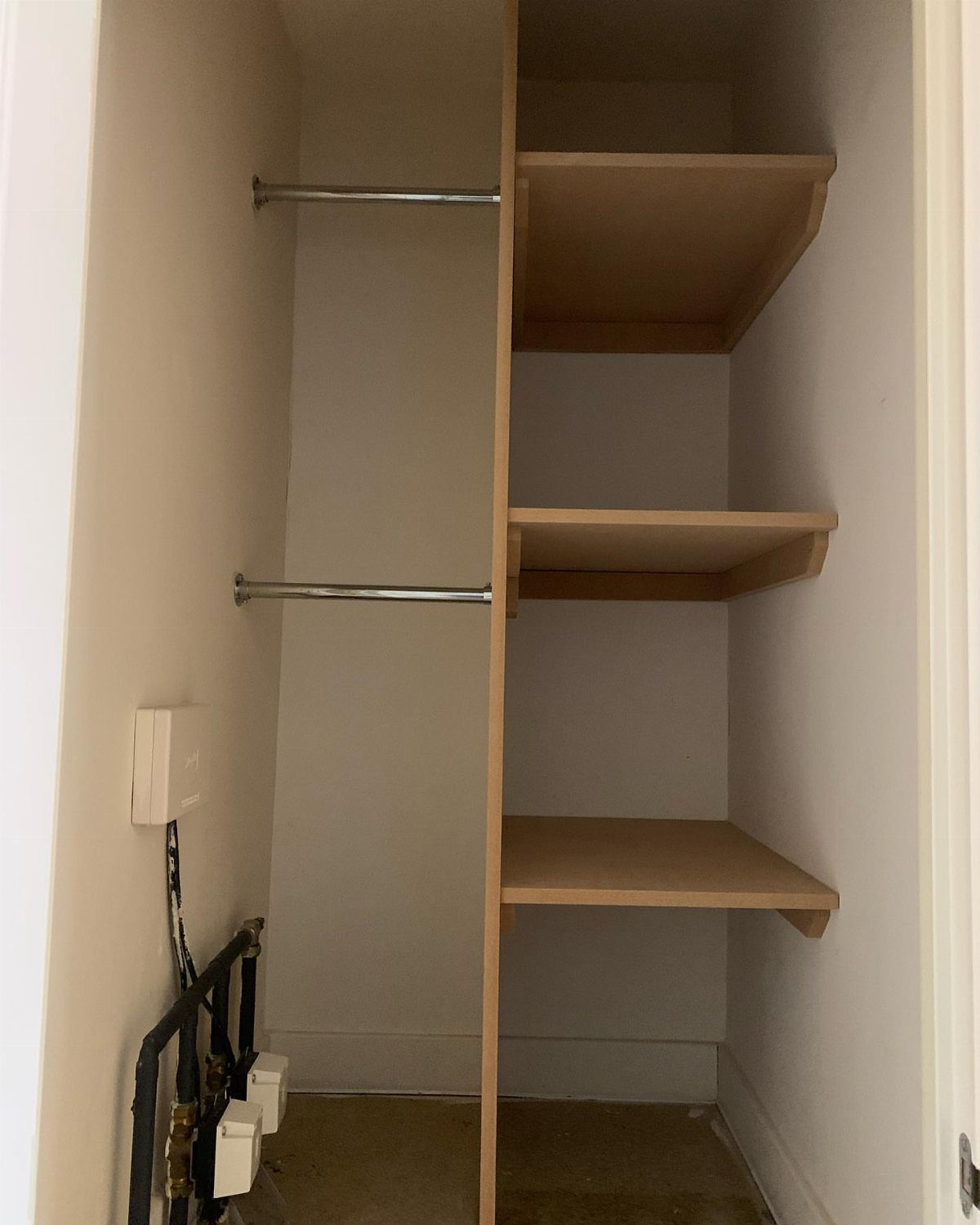 An open storage cupboard featuring two metal rails and three wooden shelves against white walls.