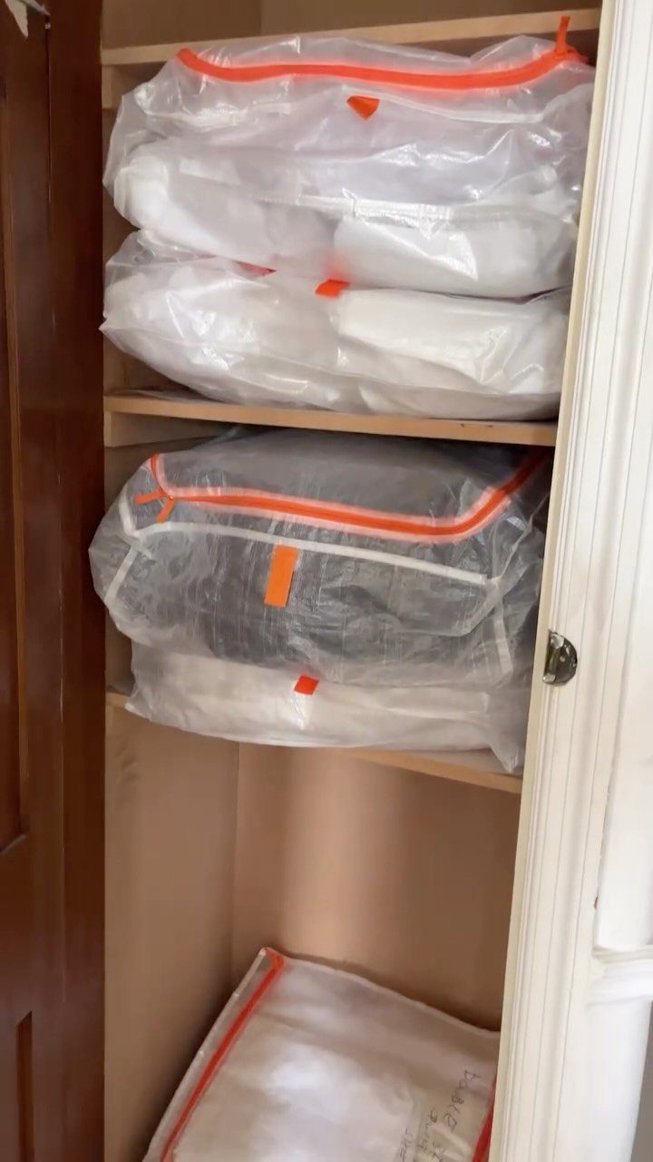 Folded linens in vacuum-seal bags stacked on wooden cupboard shelves.