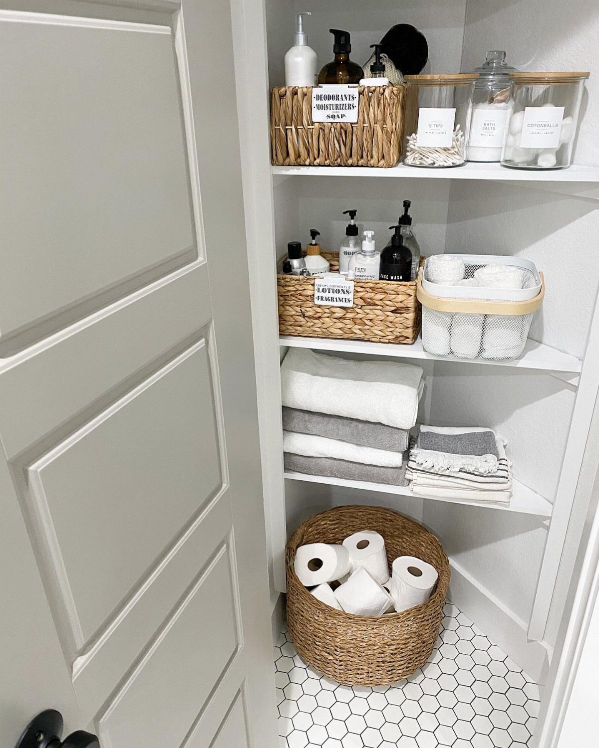Open white built-in closet shelves filled with organized baskets, jars, and folded towels.