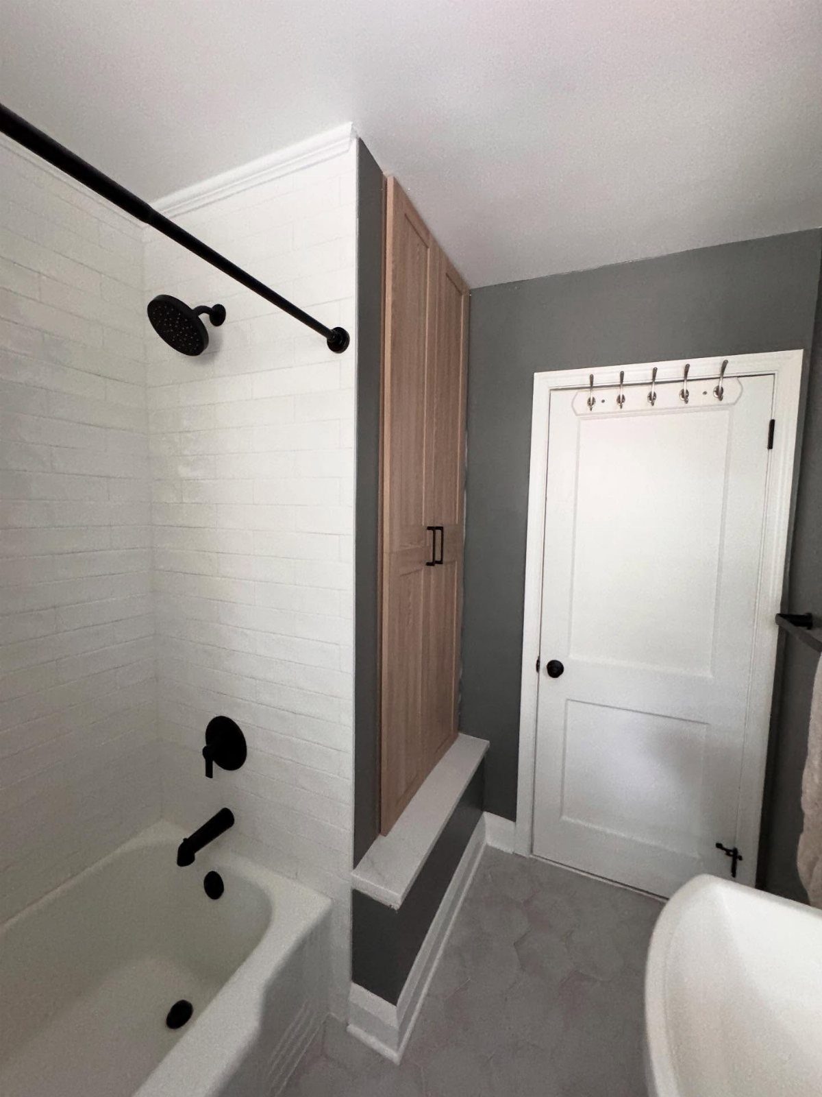 A white bathtub and shower area next to a built-in light wood closet door.