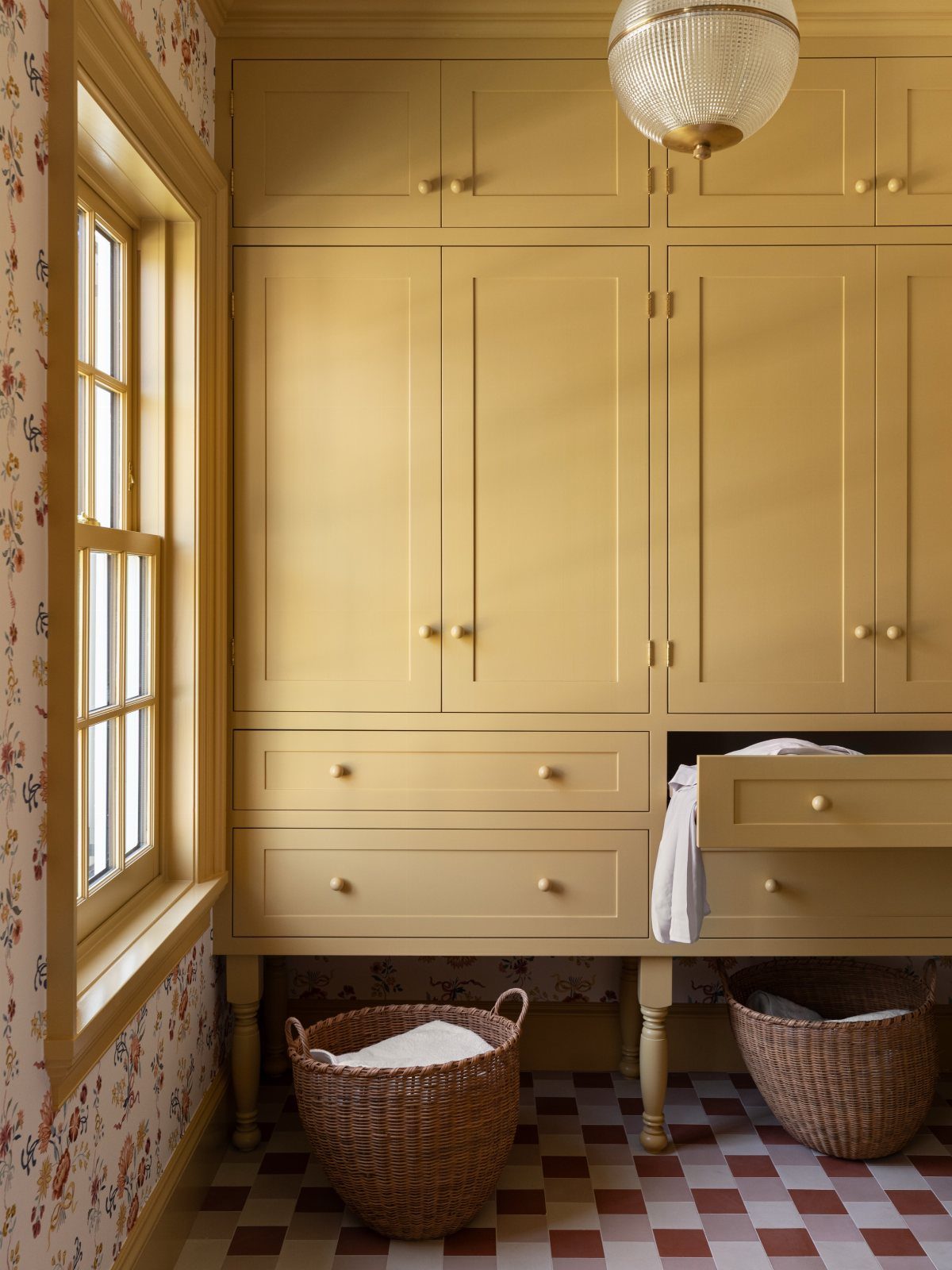 Yellow built-in bathroom cabinets with tall doors, wide drawers, and wicker baskets on a checkered floor.