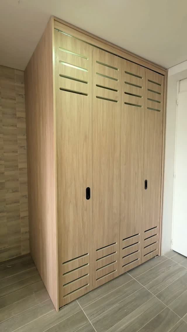 Large light wood built-in closet with slatted vent details and black handles.