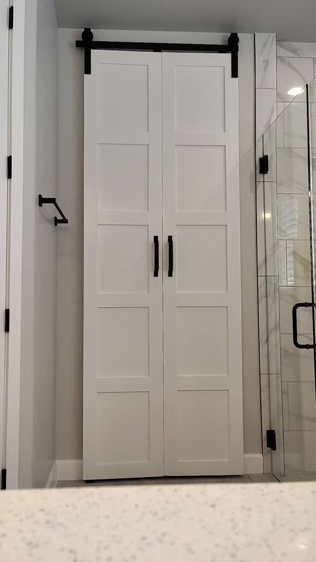 White paneled sliding barn doors with black hardware hanging on a track in a bathroom.