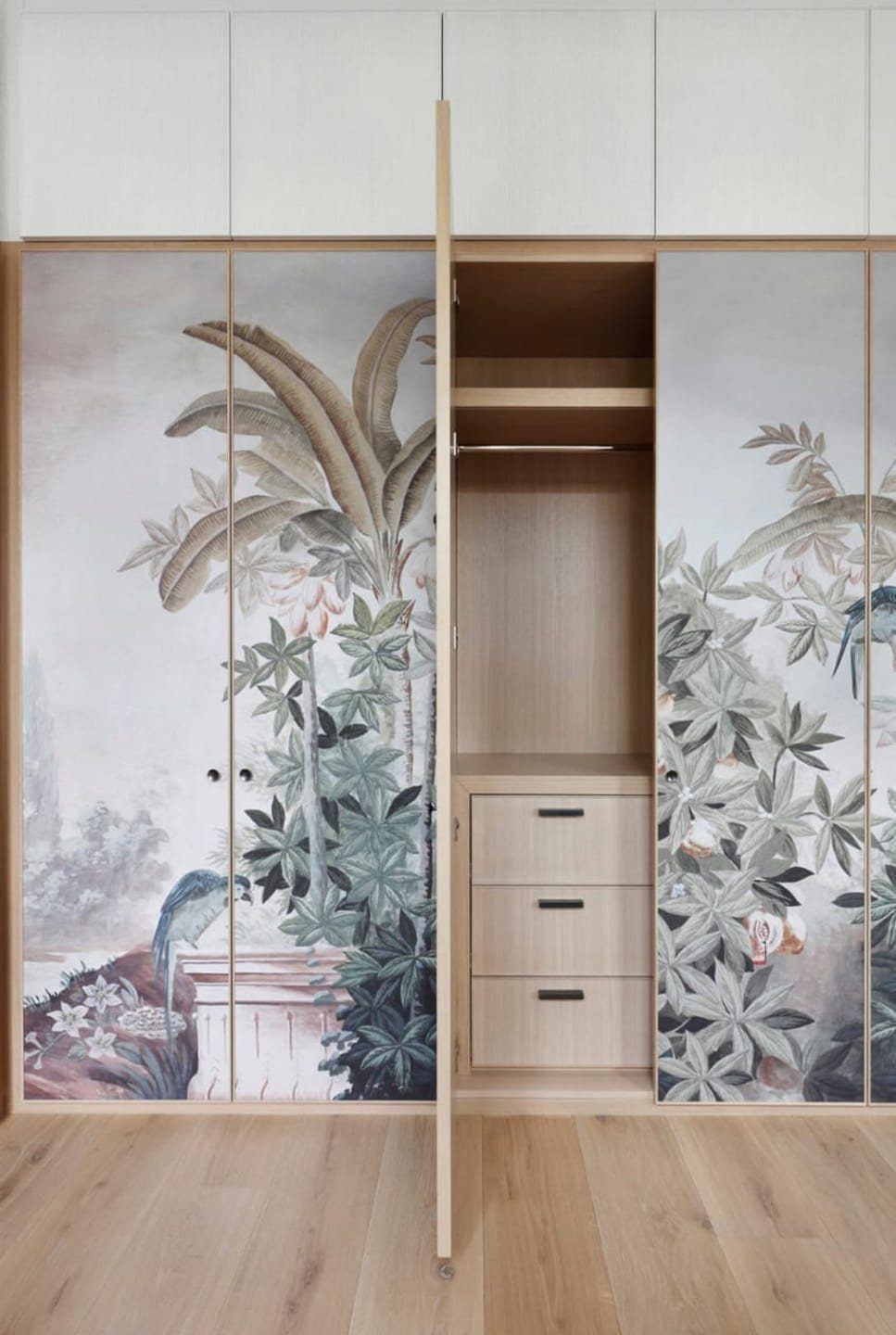 Closet doors featuring tropical botanical wallpaper pattern next to an open wooden closet interior.