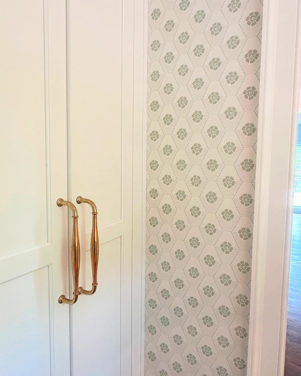 White paneled closet doors with gold handles next to patterned wallpaper.