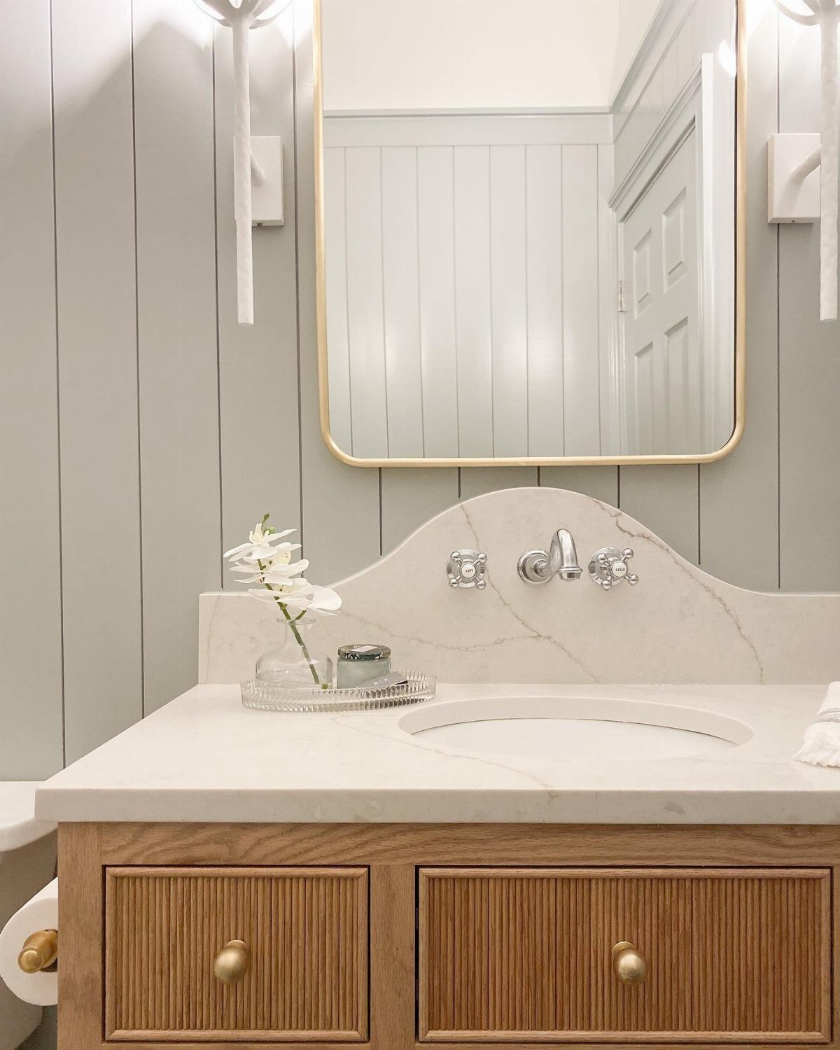White marble bathroom countertop featuring a decorative integrated arched backsplash and wooden vanity cabinet.