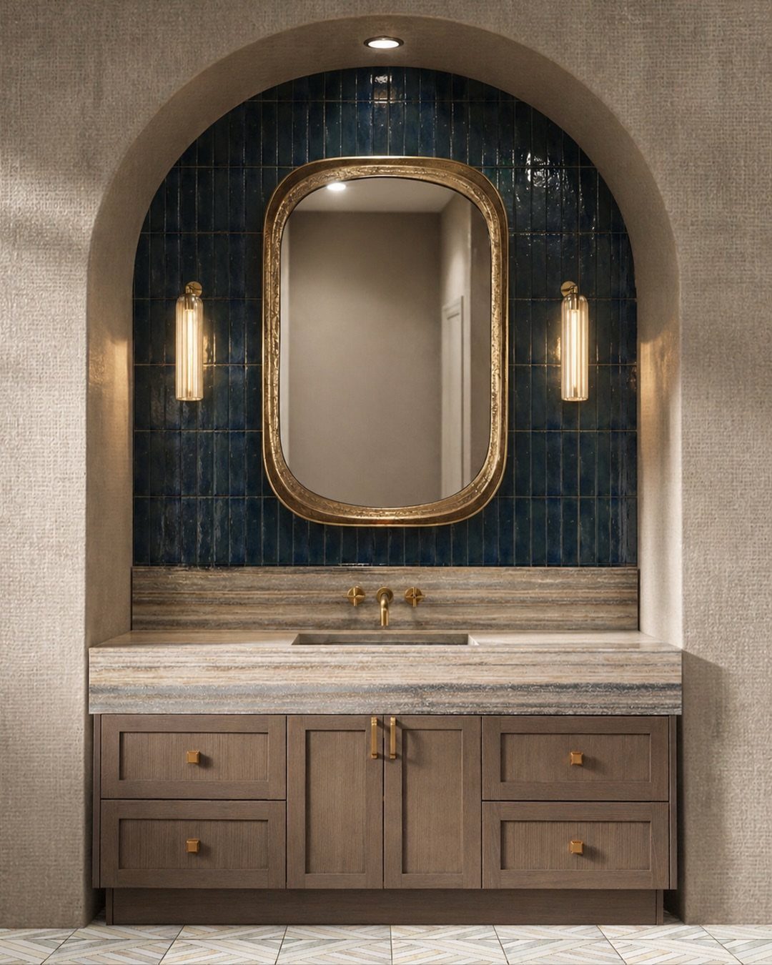 A textured stone bathroom countertop with a gold-framed mirror and blue tiled backsplash inside an arch.