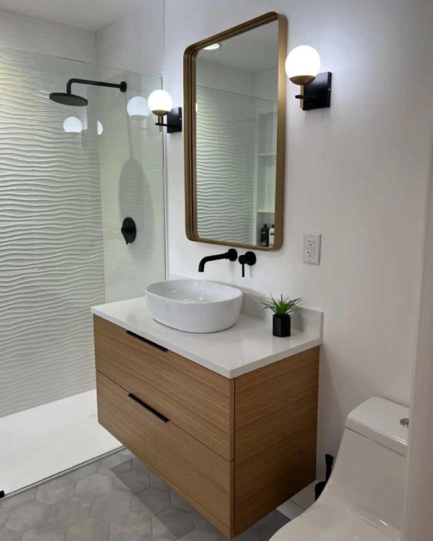 White vessel sink on a white countertop atop light wood cabinets in a modern bathroom.