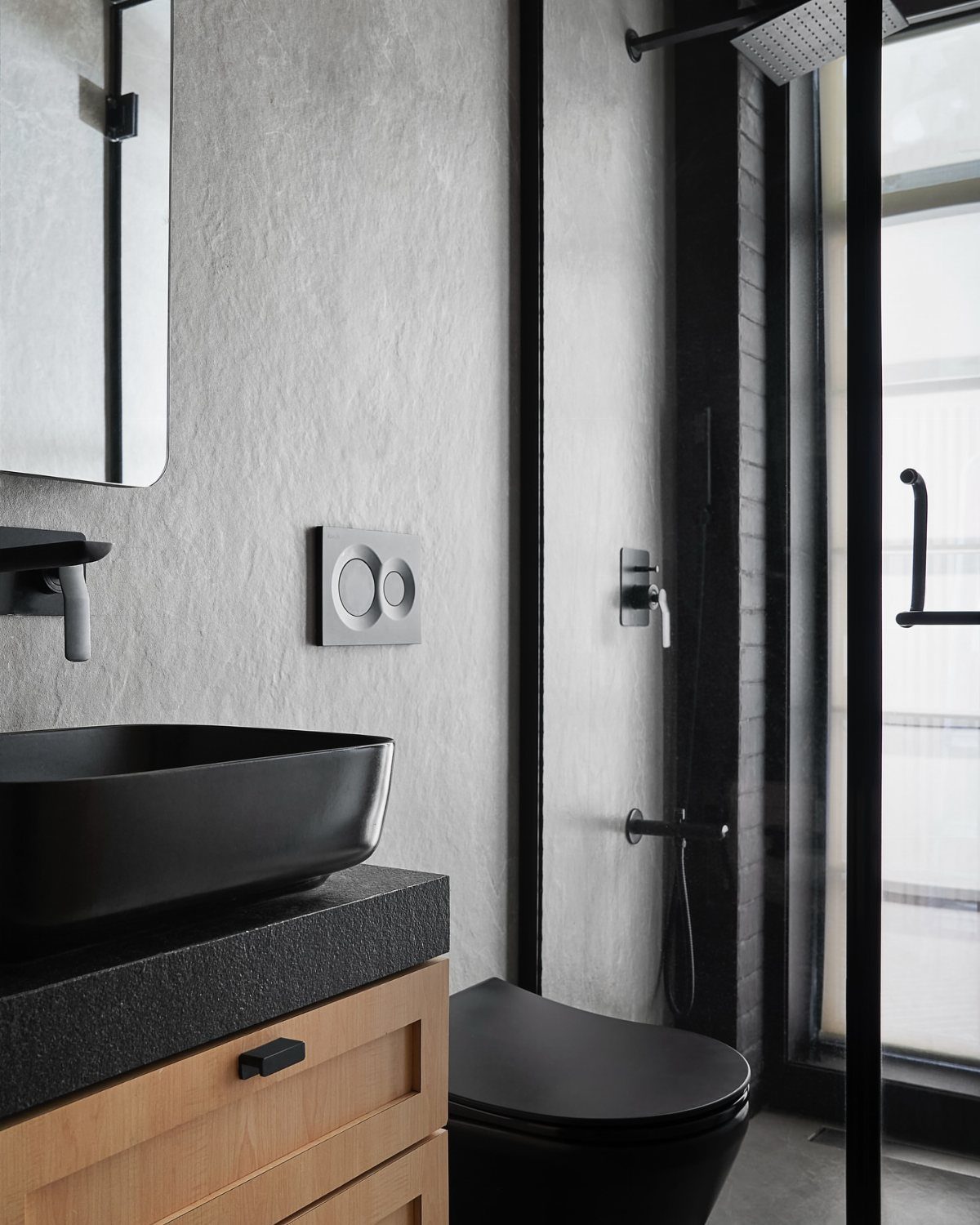 Black vessel sink on a wooden vanity next to a black toilet and walk-in shower.