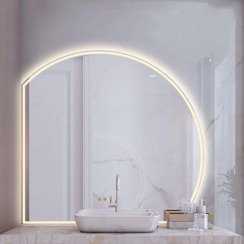 A large backlit circular mirror glowing above a white vessel sink on a marble countertop.