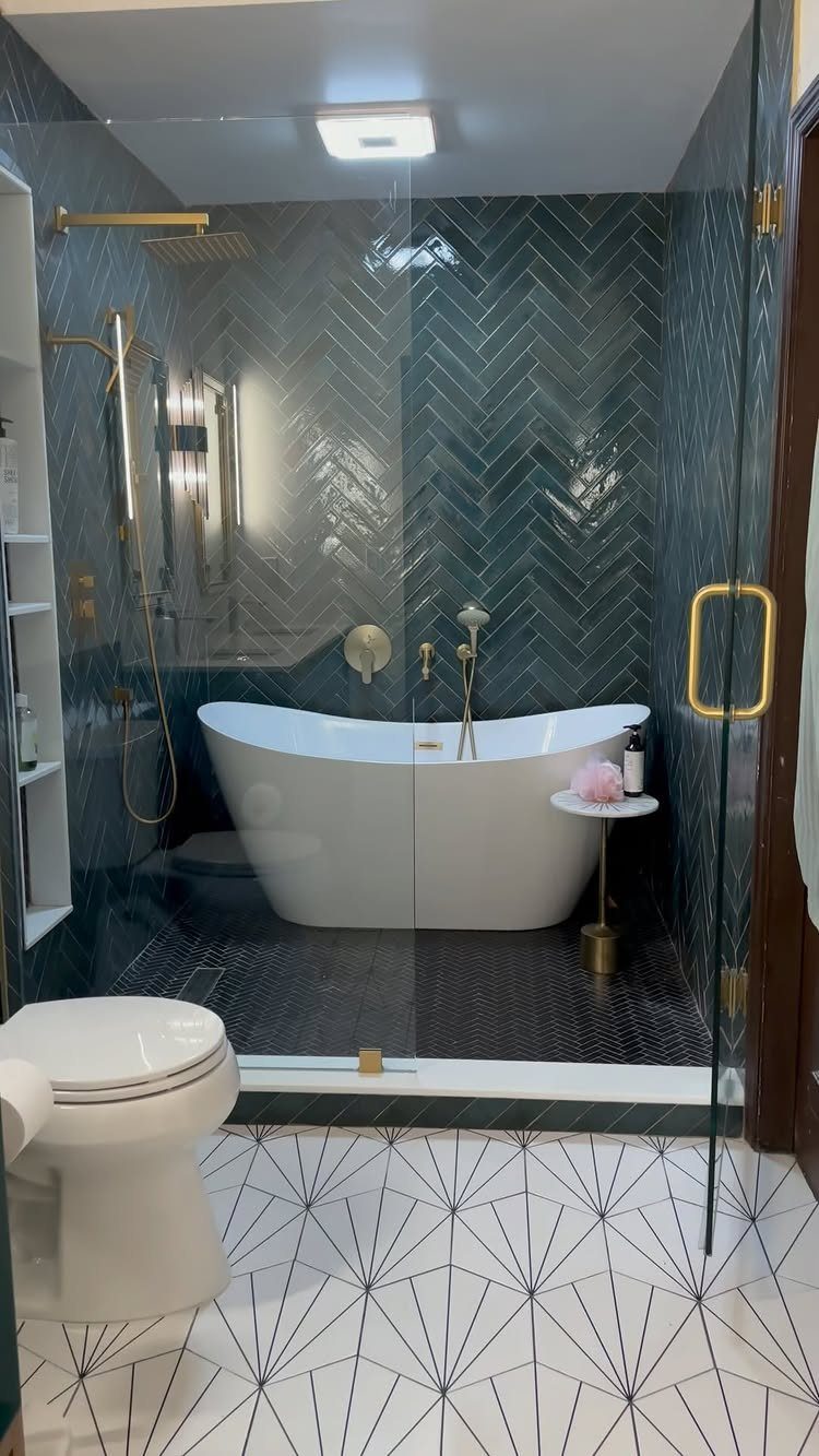 A white freestanding bathtub inside a glass-enclosed wet room with dark teal herringbone tiles.