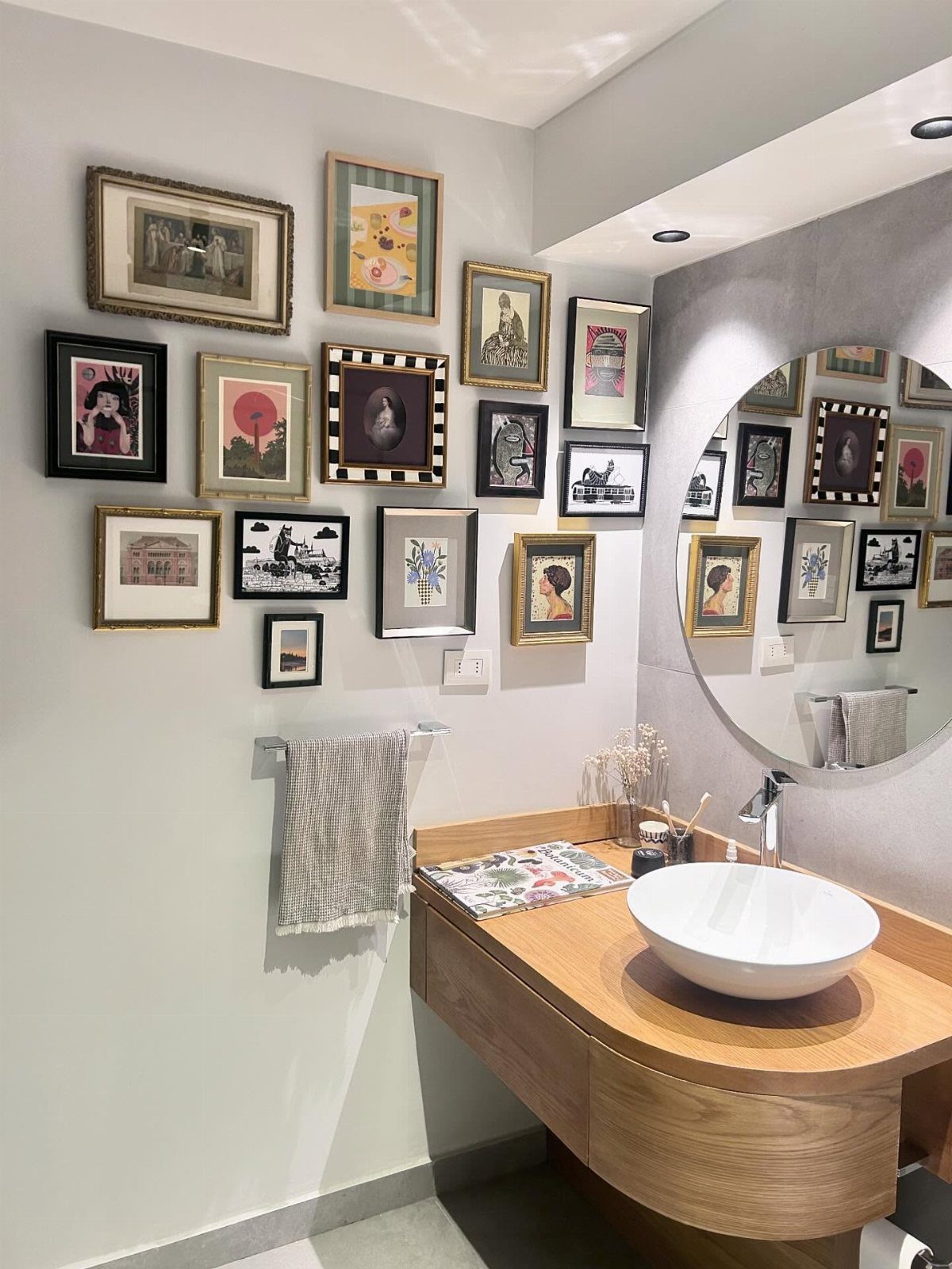 A collection of framed art pieces arranged in a gallery wall above a wooden bathroom vanity.