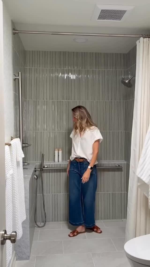 A woman standing in a tiled shower featuring installed metal grab bars on the walls.
