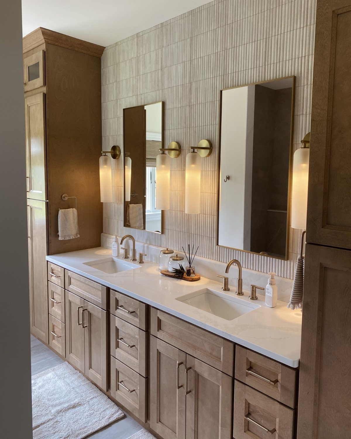 Light wood bathroom cabinets with white marble countertops and gold faucets in a modern bathroom.