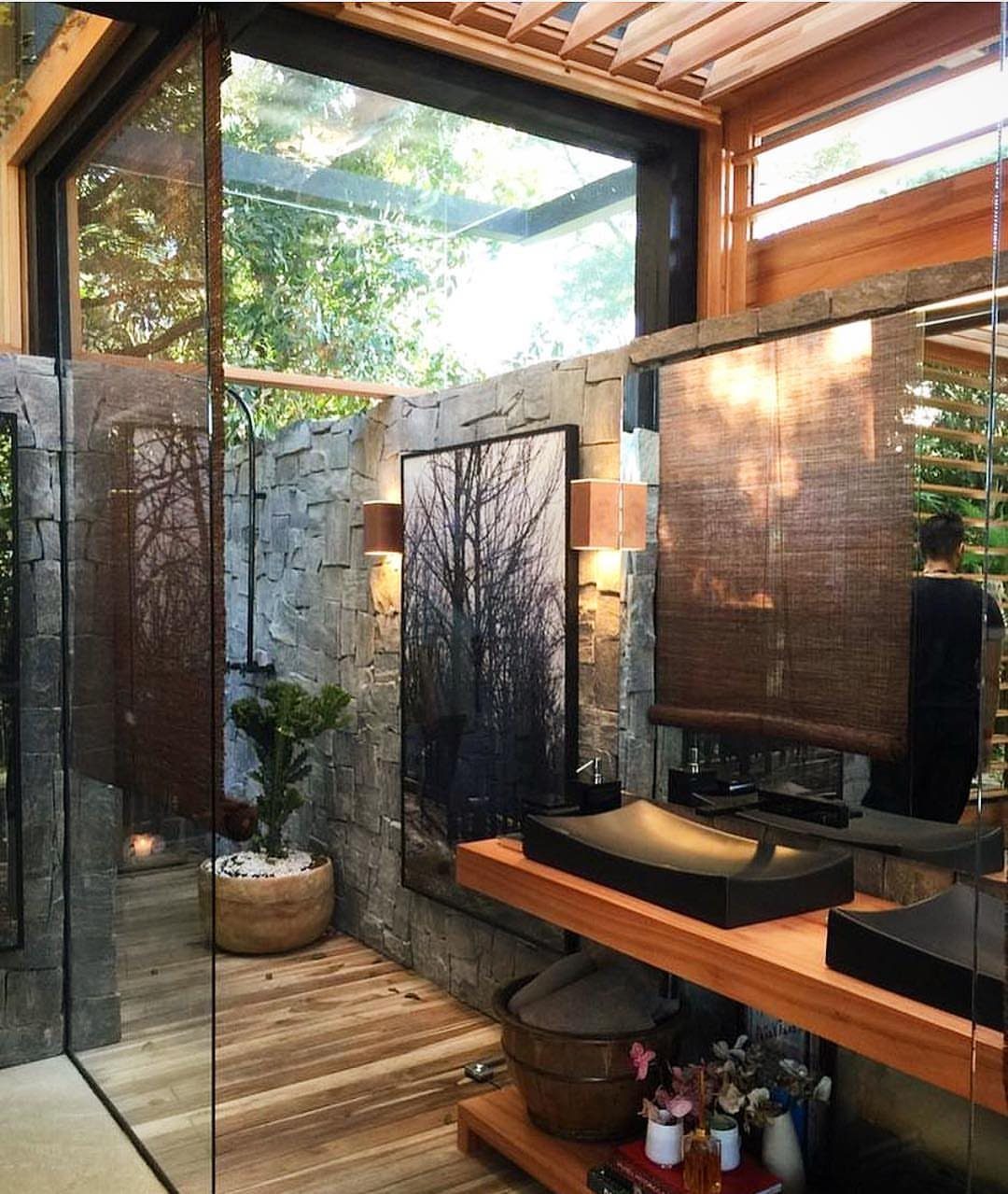 Luxury bathroom with stone walls, wooden vanity, and large windows overlooking green trees.