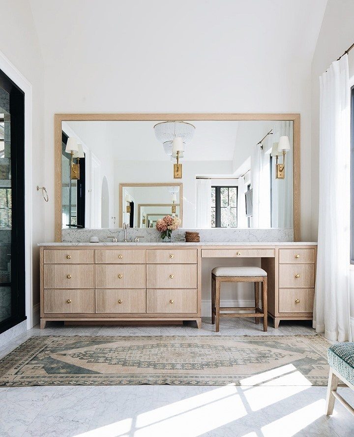 A light wood bathroom vanity with a marble countertop and a dedicated makeup station with a stool.