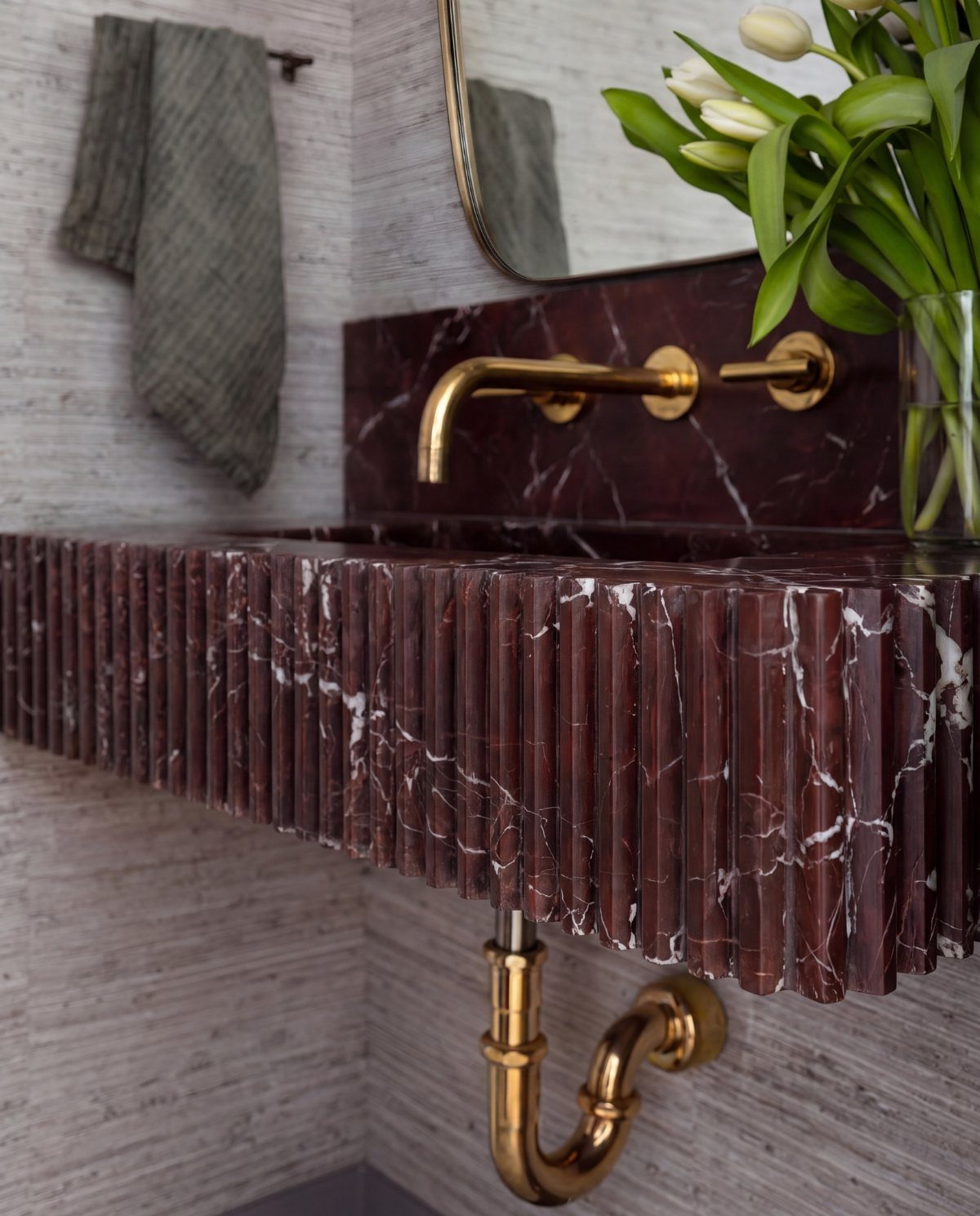 A fluted dark marble sink with gold brass fixtures and plumbing against a textured wall.