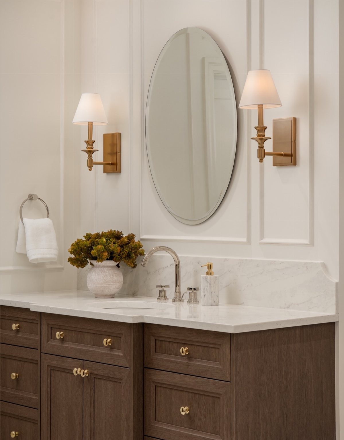 A bathroom vanity with silver faucet, gold sconces, and gold cabinet hardware on wood drawers.