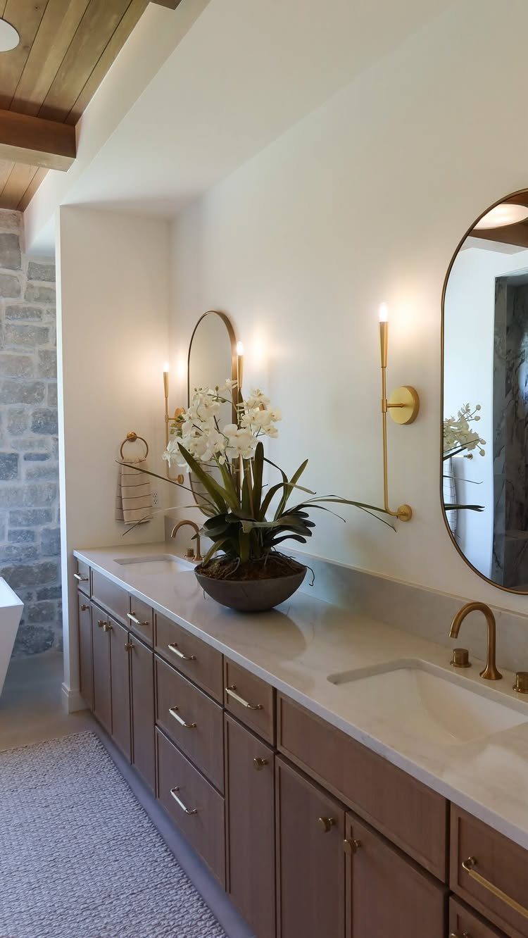 White quartz countertop with two sinks and gold faucets above wooden bathroom cabinets.