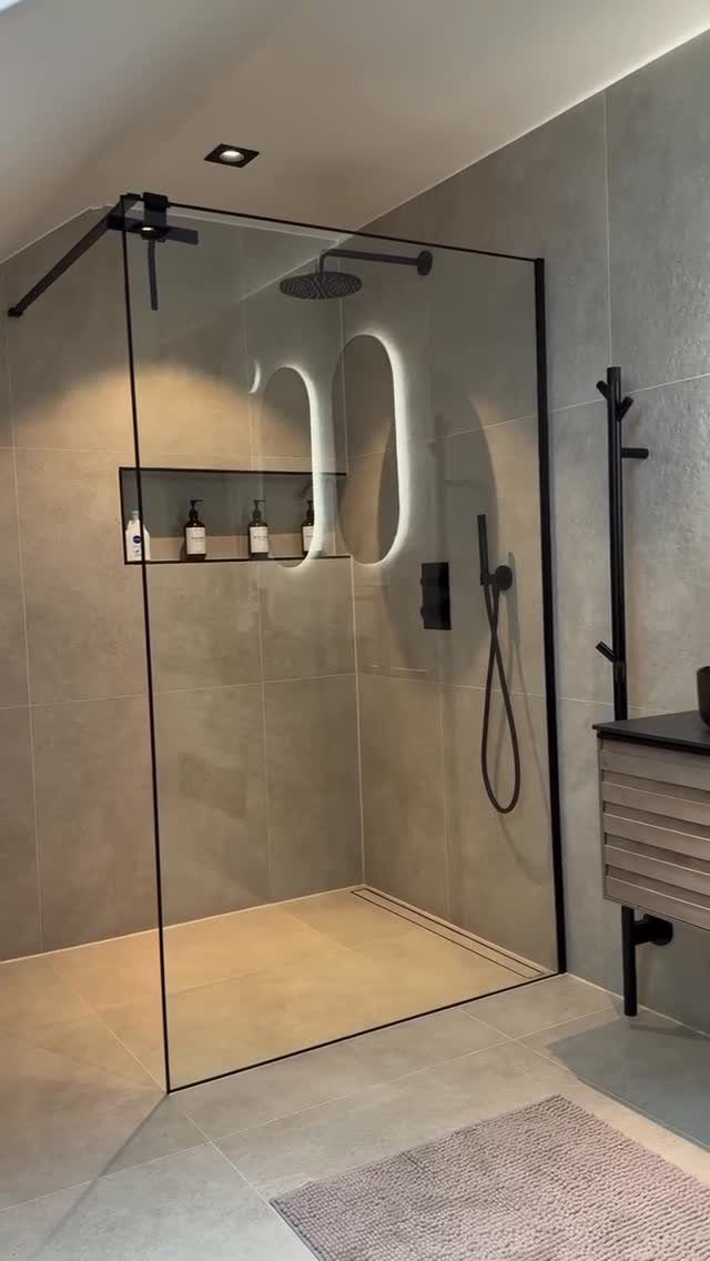 A modern walk-in shower featuring grey tiles and a black rainfall showerhead.