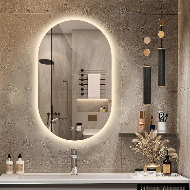 An oval backlit smart mirror mounted on a textured stone wall above a white bathroom sink.
