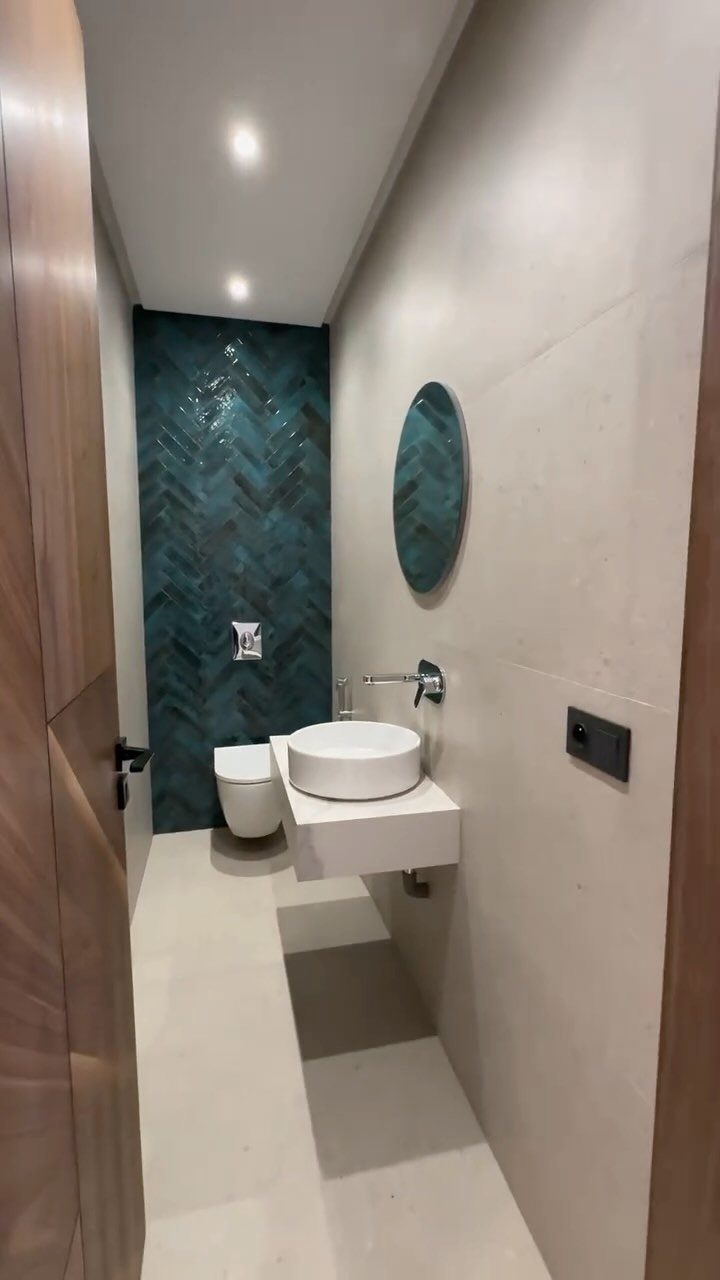 A narrow modern bathroom with a teal chevron accent wall, white vessel sink, and floating vanity.