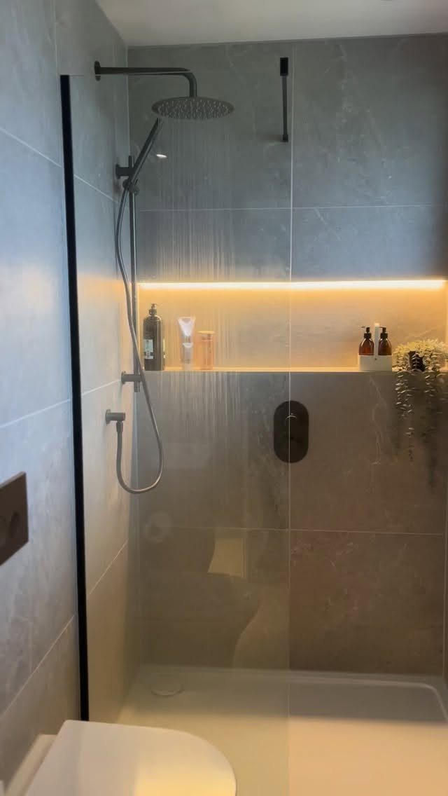 A modern walk-through shower featuring grey tiles and an illuminated horizontal wall niche.