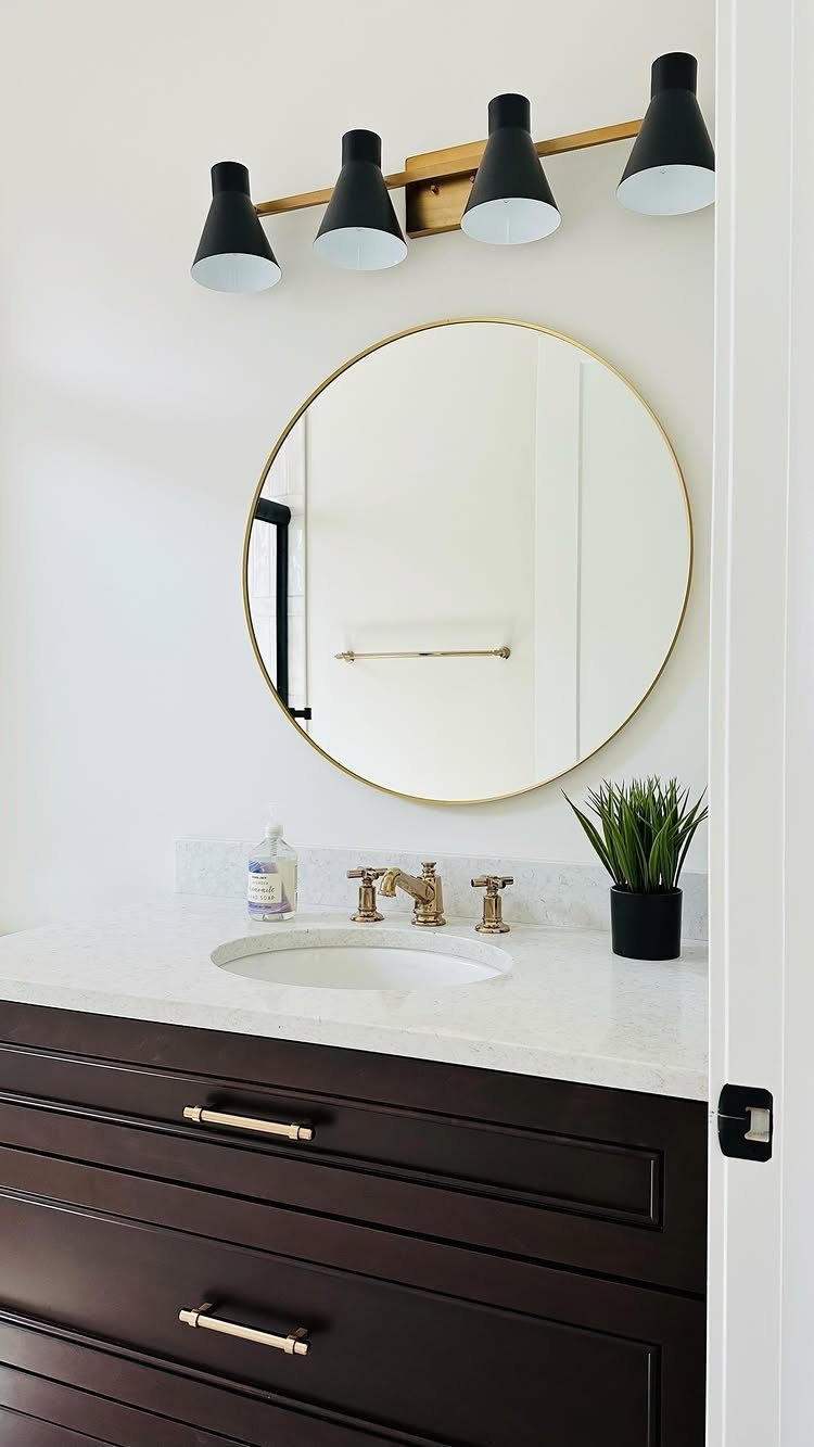 A large round gold-framed mirror hangs above a white marble bathroom vanity with gold fixtures.