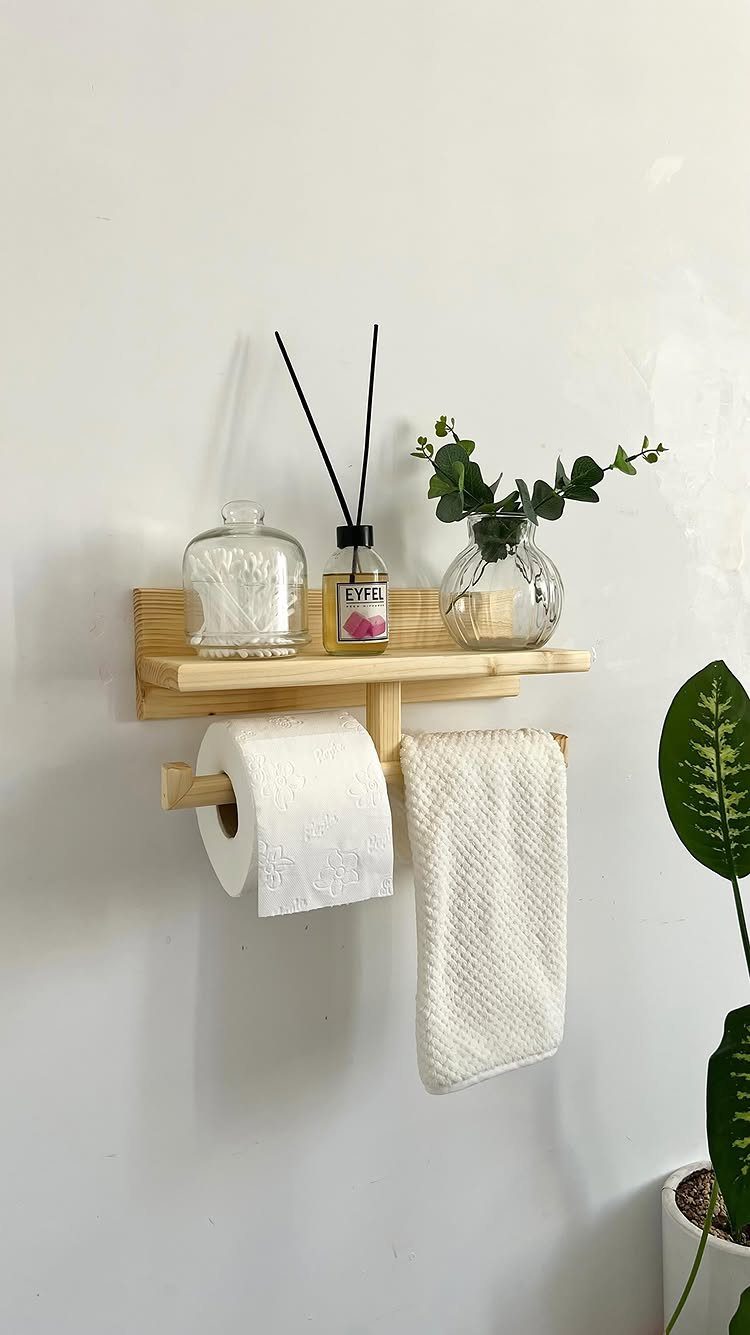 Wooden wall-mounted shelf holding a toilet paper roll and a white hand towel against a white wall.