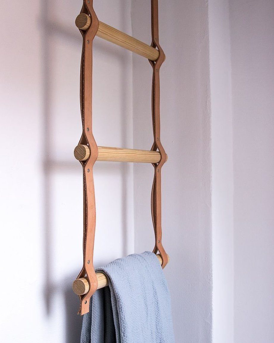 A wooden towel ladder with leather straps hanging on a white wall with a blue towel.