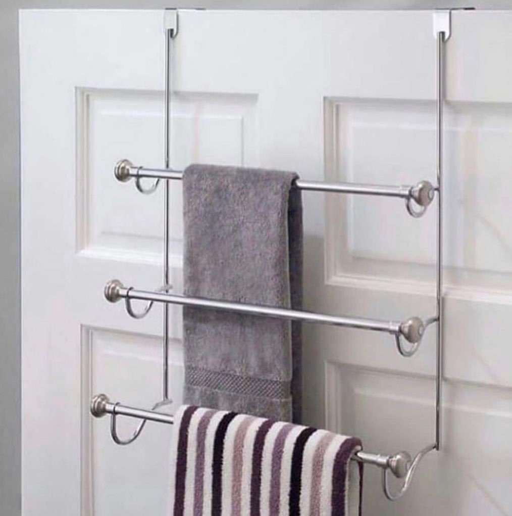 Silver metal over-the-door towel rack hanging on a white paneled door with towels.