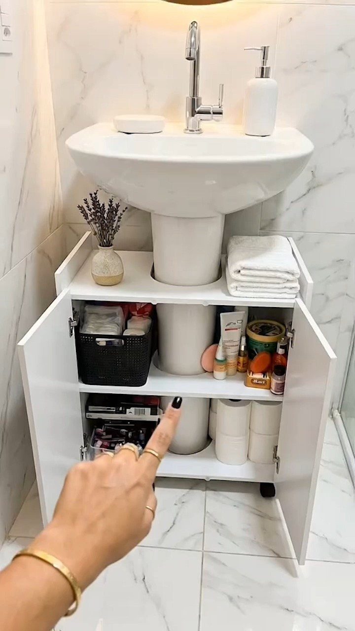 A white under-sink storage cabinet organized with baskets and toiletries beneath a pedestal sink.
