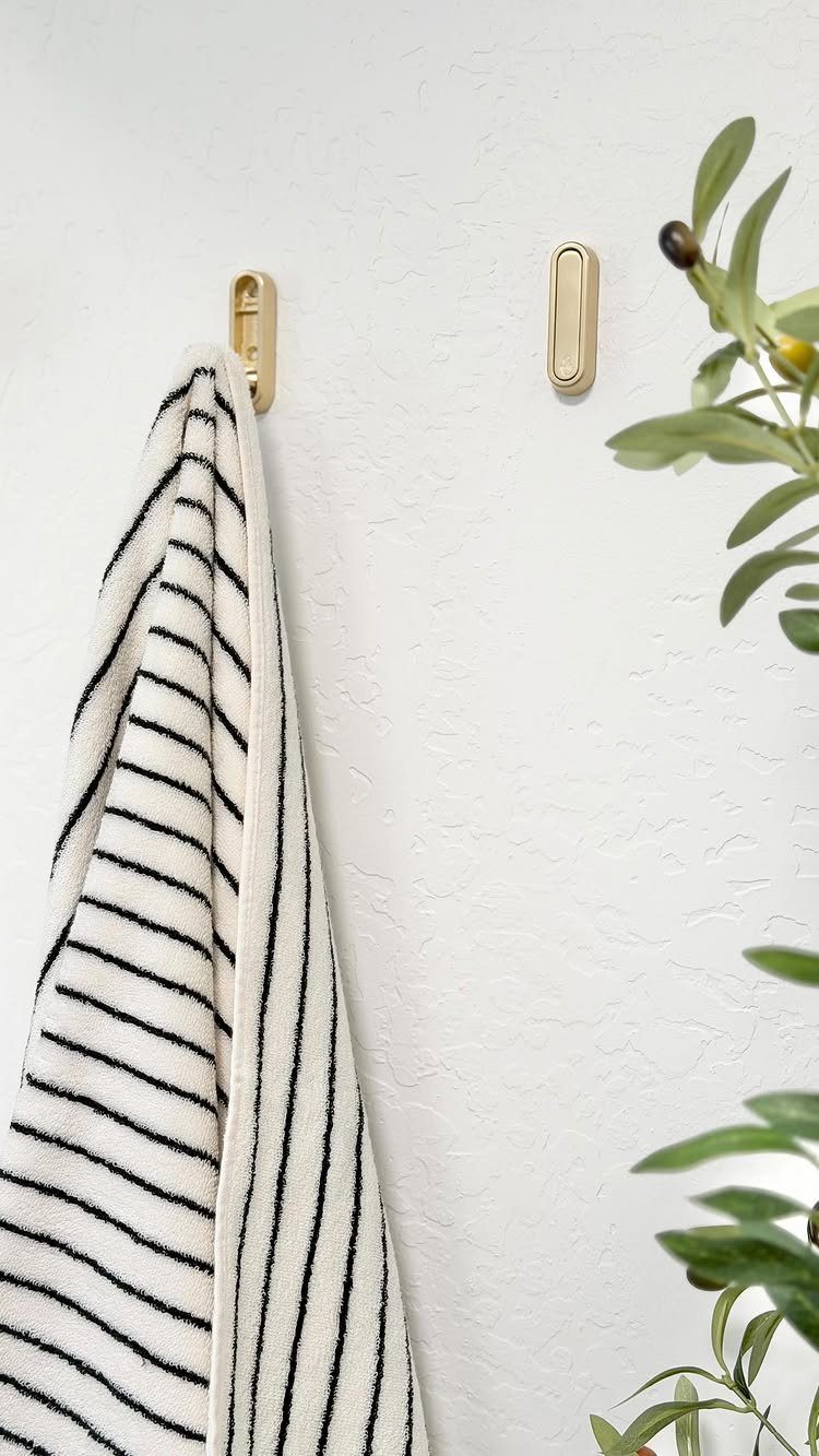 A striped white towel hanging from a gold oval hook on a white wall.