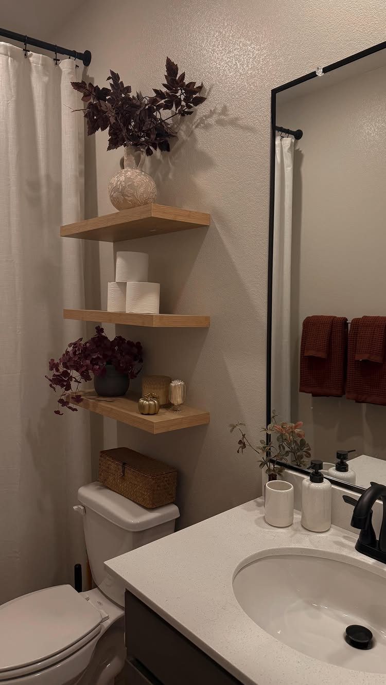 Three wooden floating shelves mounted on a beige wall holding decorative vases and candles.