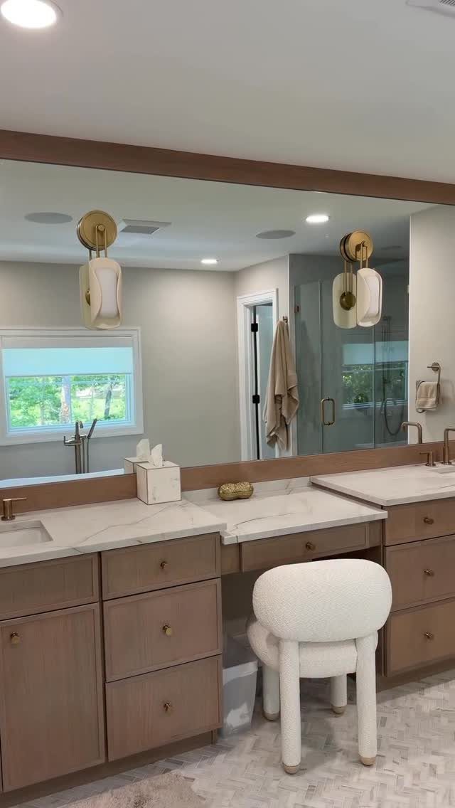 A light wood bathroom vanity with a marble countertop and a dedicated makeup station with a white stool.