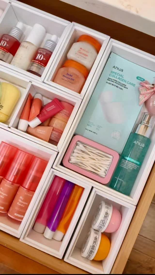 Skincare bottles and jars neatly organized in white drawer dividers within a wooden vanity drawer.
