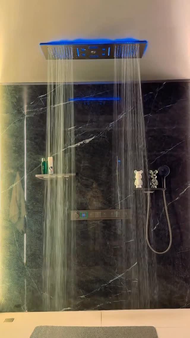 A modern rainfall showerhead with blue lighting and water streams against dark marble walls.