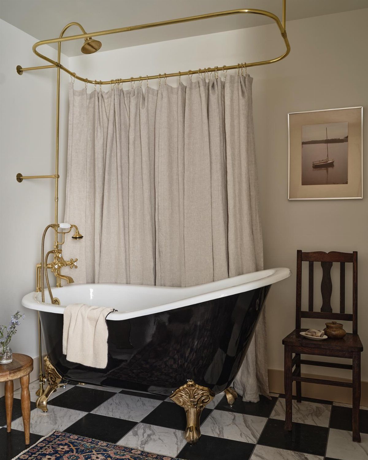 A black painted clawfoot bathtub with gold hardware on a checkered floor.