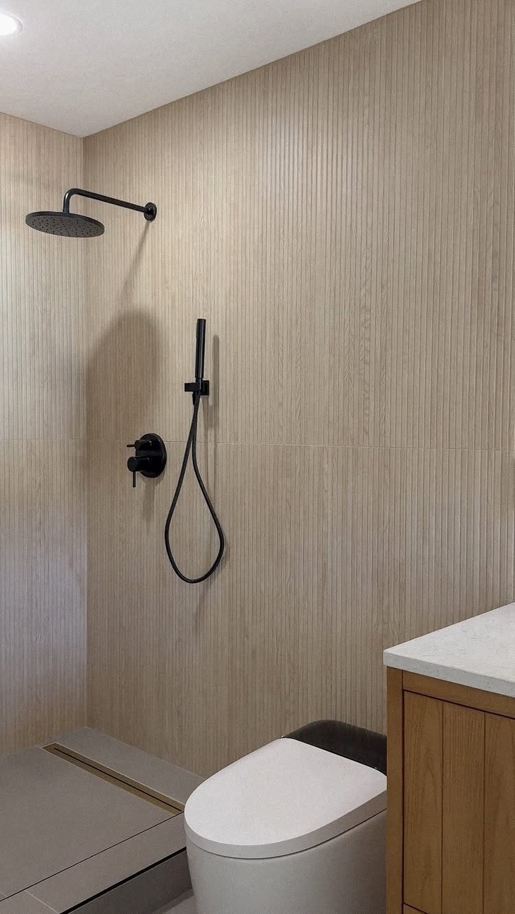 Light beige wood-look porcelain tiles covering the walls of a modern bathroom with black fixtures.