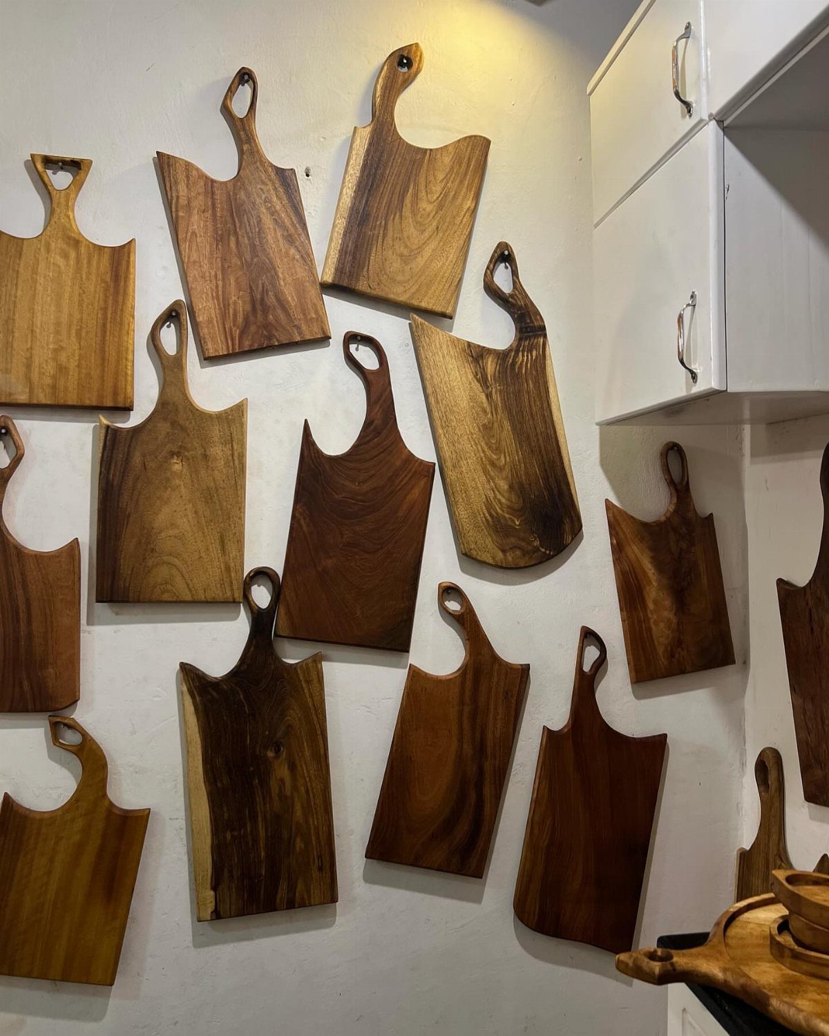 Various wooden cutting boards hanging on a white wall using hooks.