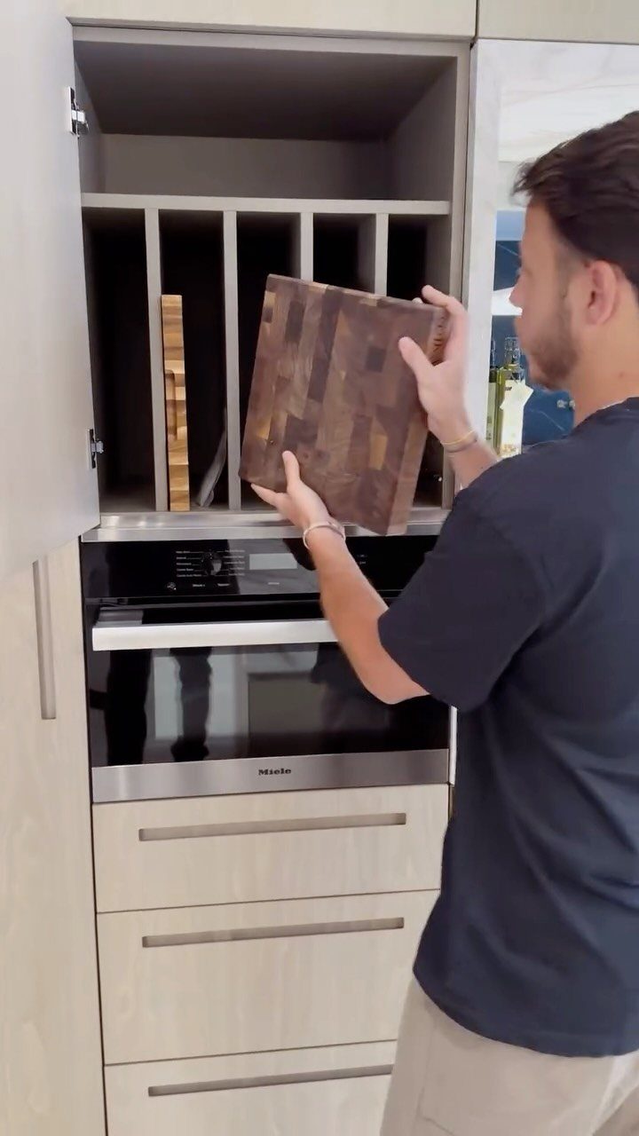 A man placing a wooden chopping board into a kitchen cabinet with vertical storage dividers.