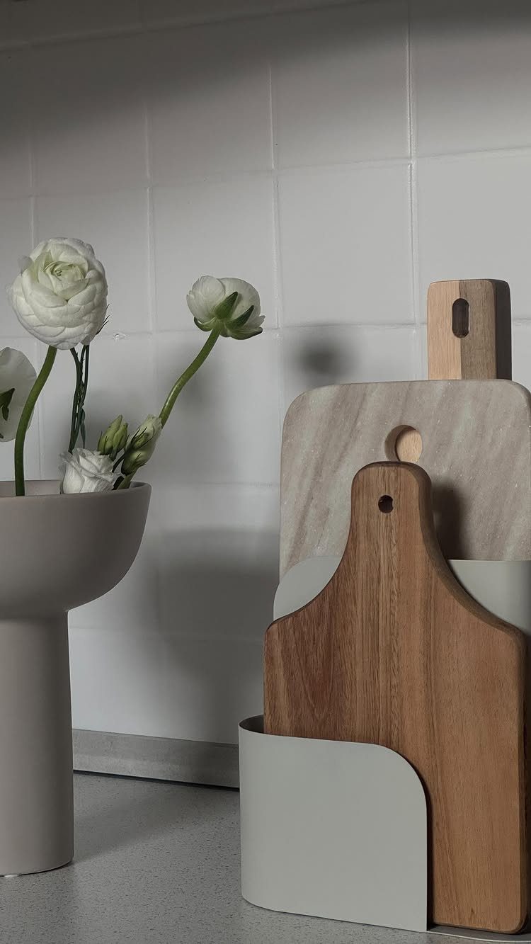 Wooden cutting boards stored upright inside a light grey magazine holder on a kitchen countertop.