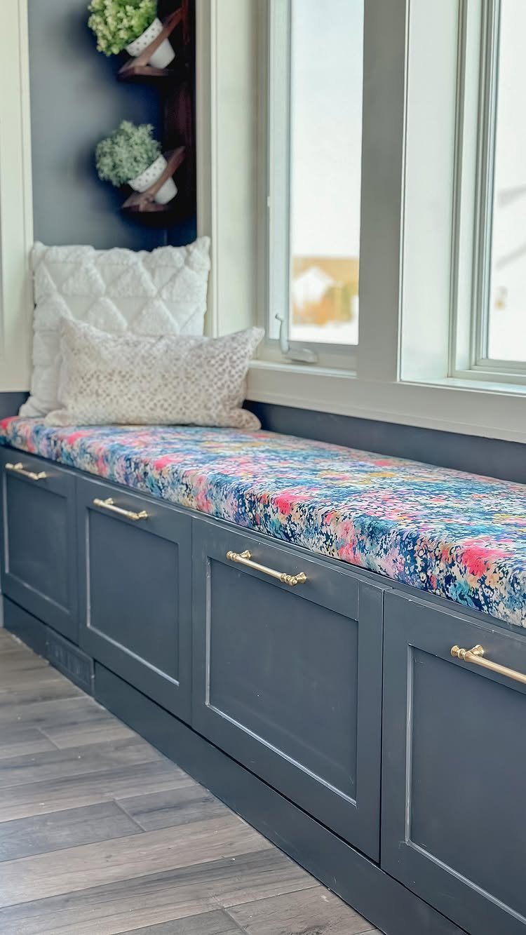 Built-in window bench with blue cabinetry, floral cushion, and white pillows near a window.