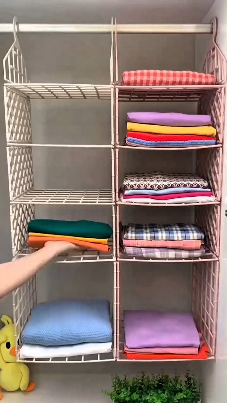 Pink wire mesh hanging organizer with cubbies filled with folded colorful clothing hanging from a rod.