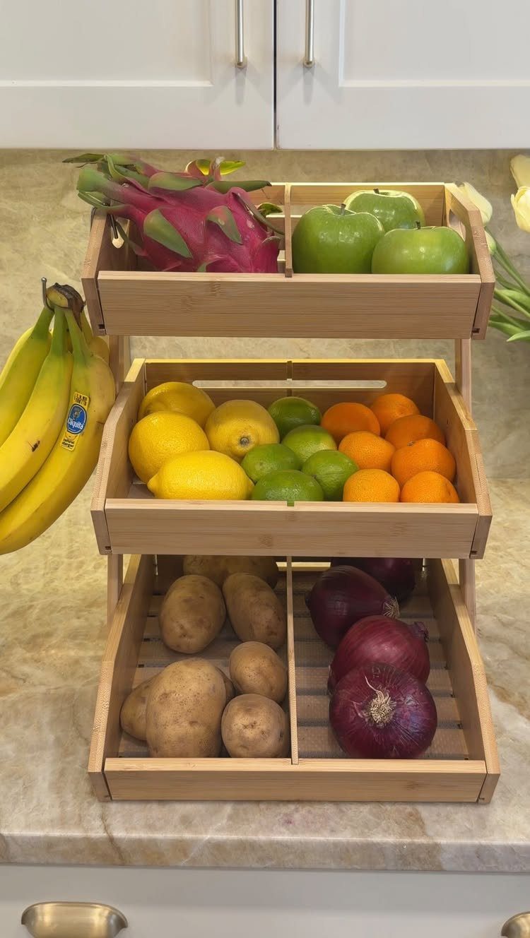 Three-tiered wooden fruit basket filled with various colorful fruits and vegetables on a marble counter.