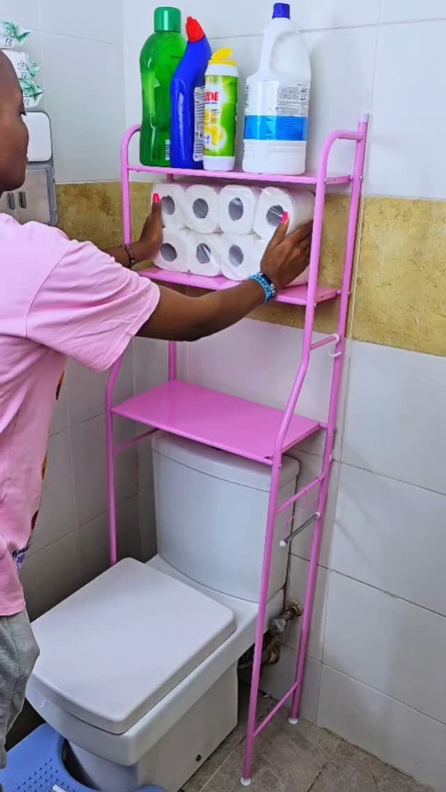 A person reaching for toilet paper rolls on a pink metal storage rack above a toilet.